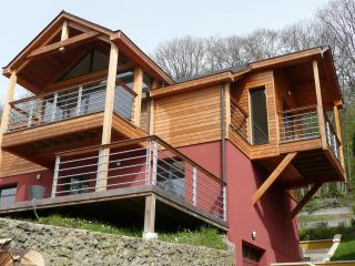 Surélévation en ossature bois, bardage en bois naturel, toiture double pente en ardoise, balcons et garde-corps métalliques, arbalétriers apparents.