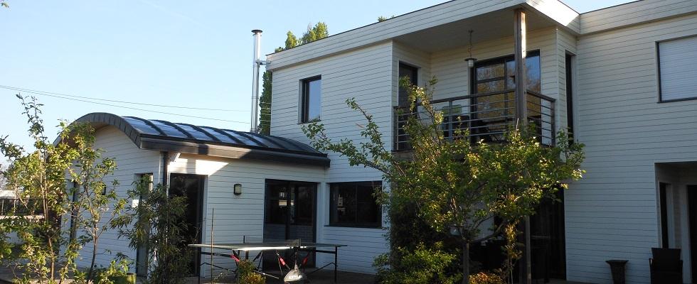 Maison en ossature bois sur deux niveaux, bardage peint, toit en voûte, balcon.