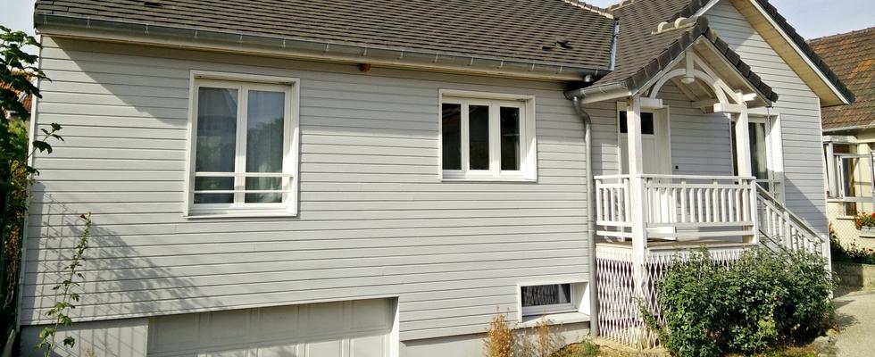 Maison en ossature bois, bardage peint, toiture en ardoise, porche d'entrée, garage en sous-sol.