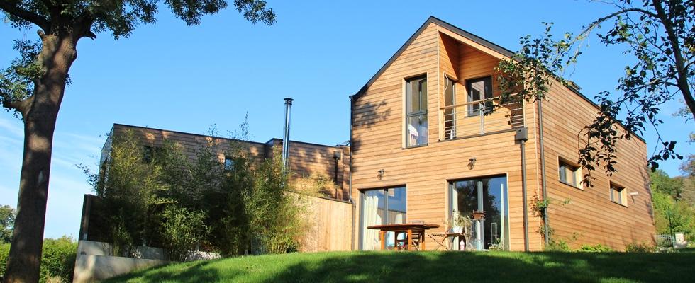 Maison en ossature bois, bardage en bois naturel, baies vitrées, balcon, garde-corps métallique.