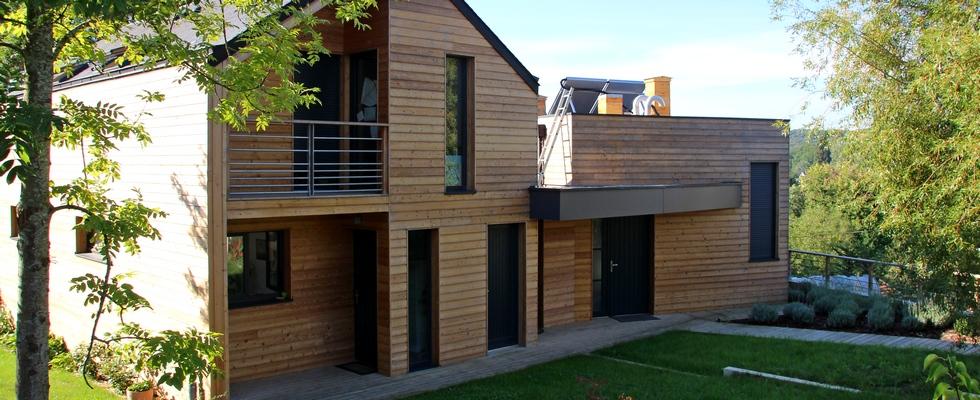 Maison en ossature bois, bardage en bois naturel, baies vitrées, balcon, garde-corps métallique.