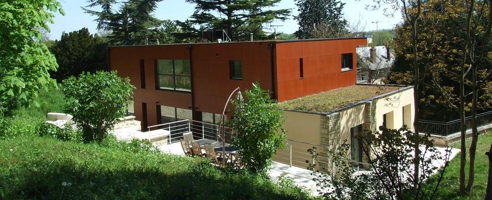 Extension en ossature bois, panneaux de résine, toiture végétalisée, terrasse avec garde-corps métallique.